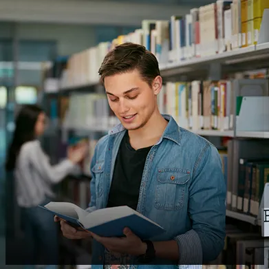 Młody mężczyzna z uśmiechem czyta książkę w bibliotece